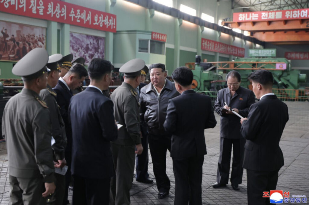 Screenshot 20260510 at 3 30 34 pm | nk insider group of officials in military uniforms and suits listen to a man in a gray jacket speaking inside a factory with workers taking notes and large machinery in the background